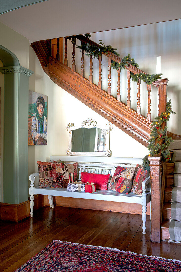 Wooden banister with antique bench and Moroccan cushions in Grade II listed Georgian country house West Sussex UK