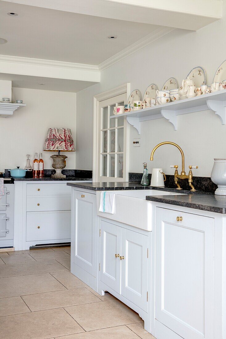Weiße und hellblaue Küche mit dunkelgrauer Arbeitsplatte und offenen Regalen mit altem Porzellan in einem eleganten Haus in Hampshire, Großbritannien
