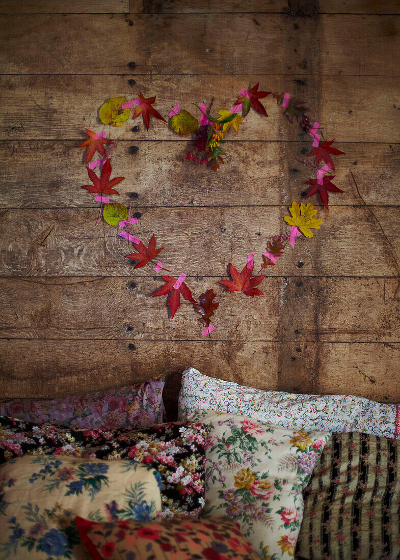 Herz aus Blättern über verschiedenen Blumenkissen in rustikaler Holzhütte Herbst UK
