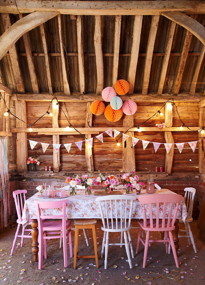 Pinkfarbene Stühle und Stufenkuchen mit Wimpeln und Lichtern in einer Holzhütte im Spätsommer UK