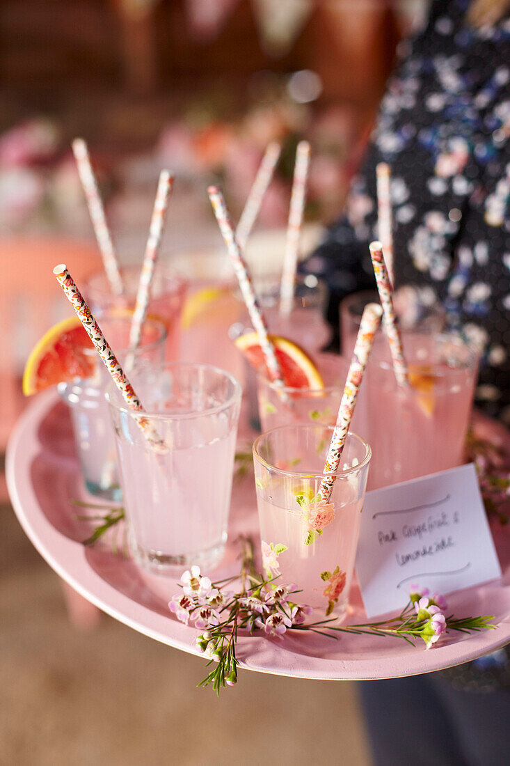 Woman carrying tray with pink grapefruit lemonade in glasses with straws