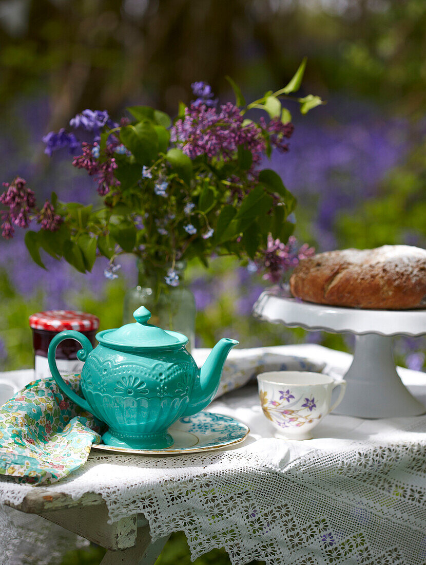 Turquoise teapot and cake with cut flowers on table in bluebell woods
