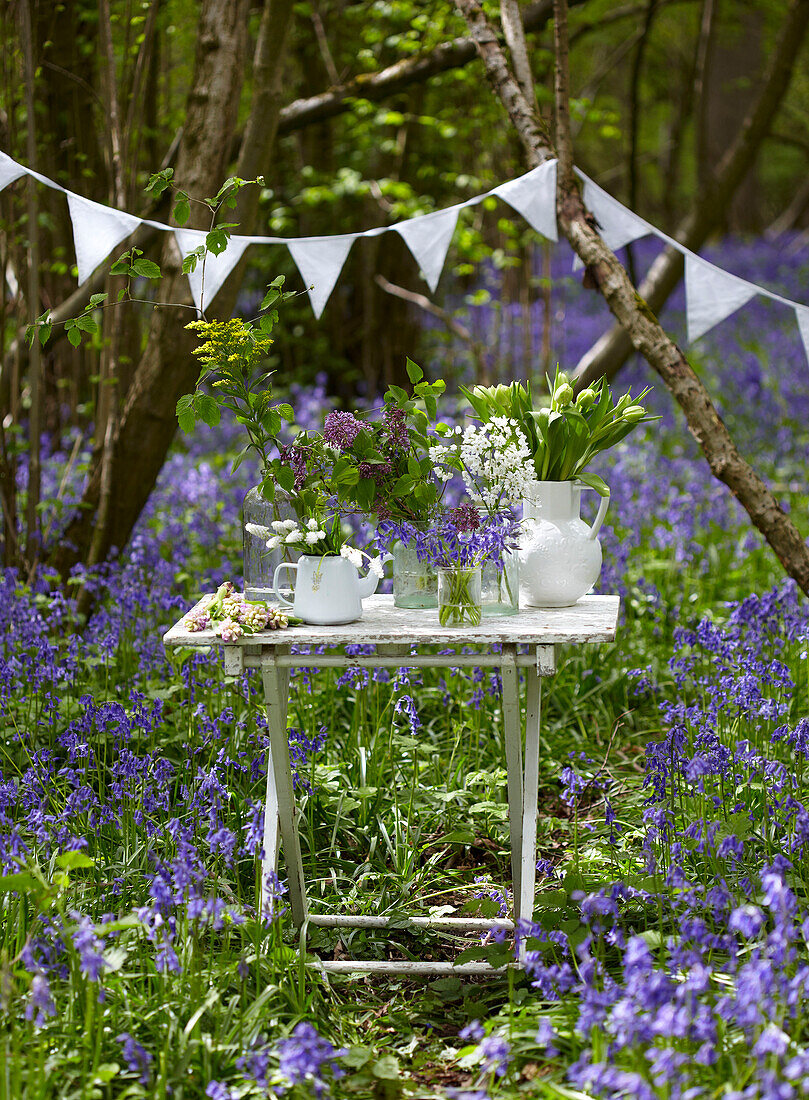 Cut flowers on table with bunting in bluebell woods (Hyacinthoides non-scripta)