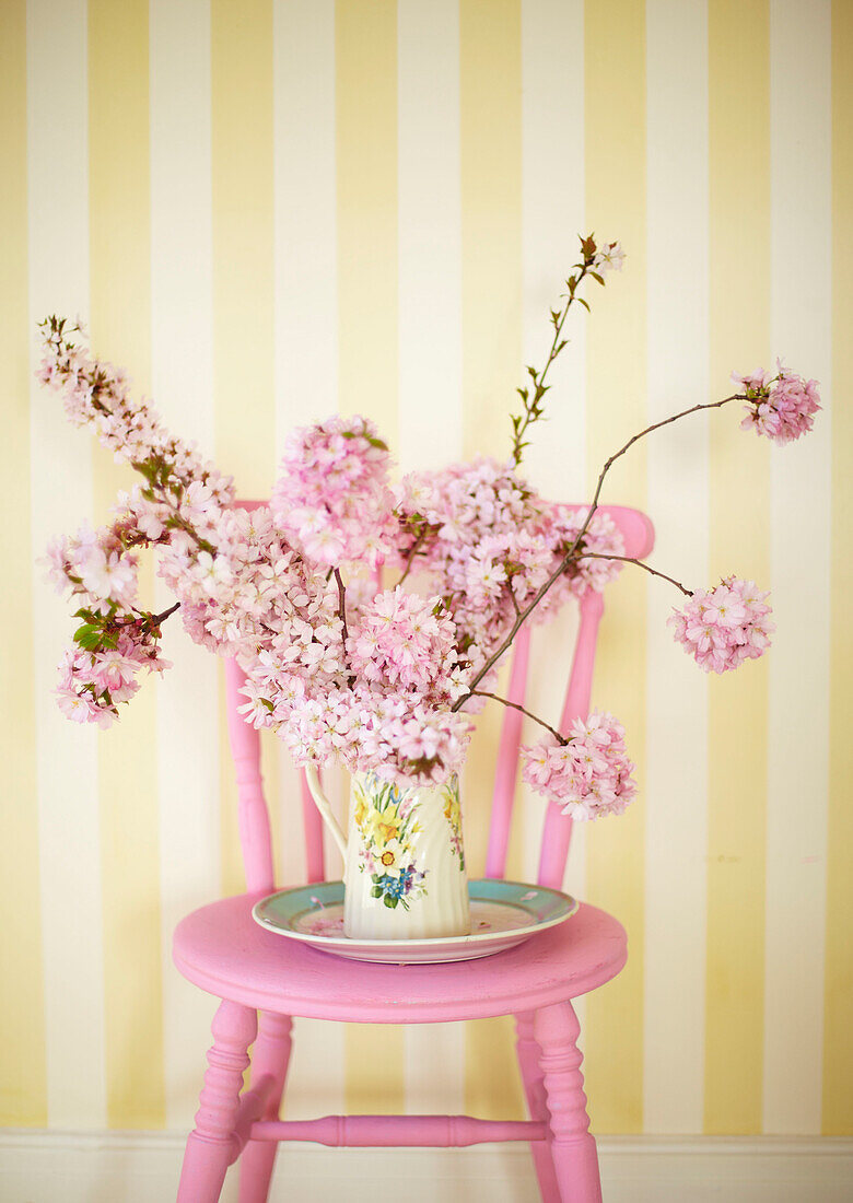 Frühlingsblüten auf einem rosa gestrichenen Stuhl mit gestreifter gelber Tapete