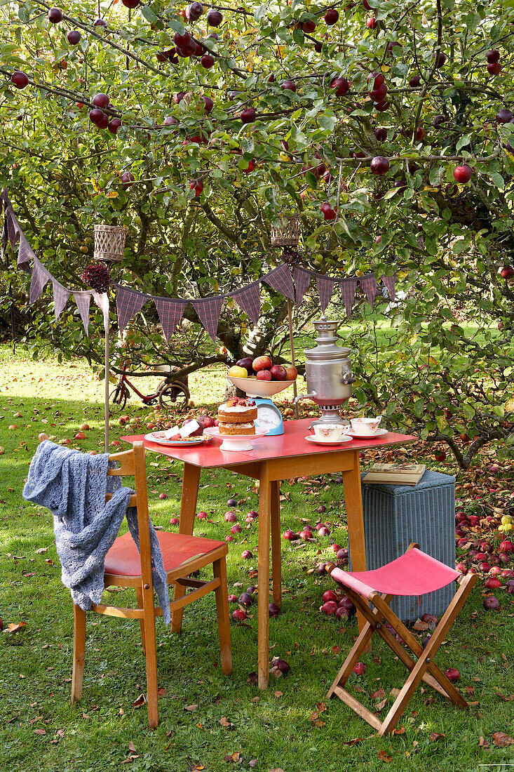 Roter Tisch und Stühle unter einem Apfelbaum mit Fähnchen im Garten auf der Isle of Wight, Großbritannien