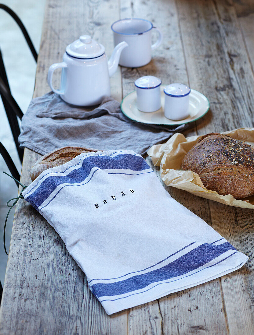 Linen bread bag on wooden table top with enamelware teapot and mug