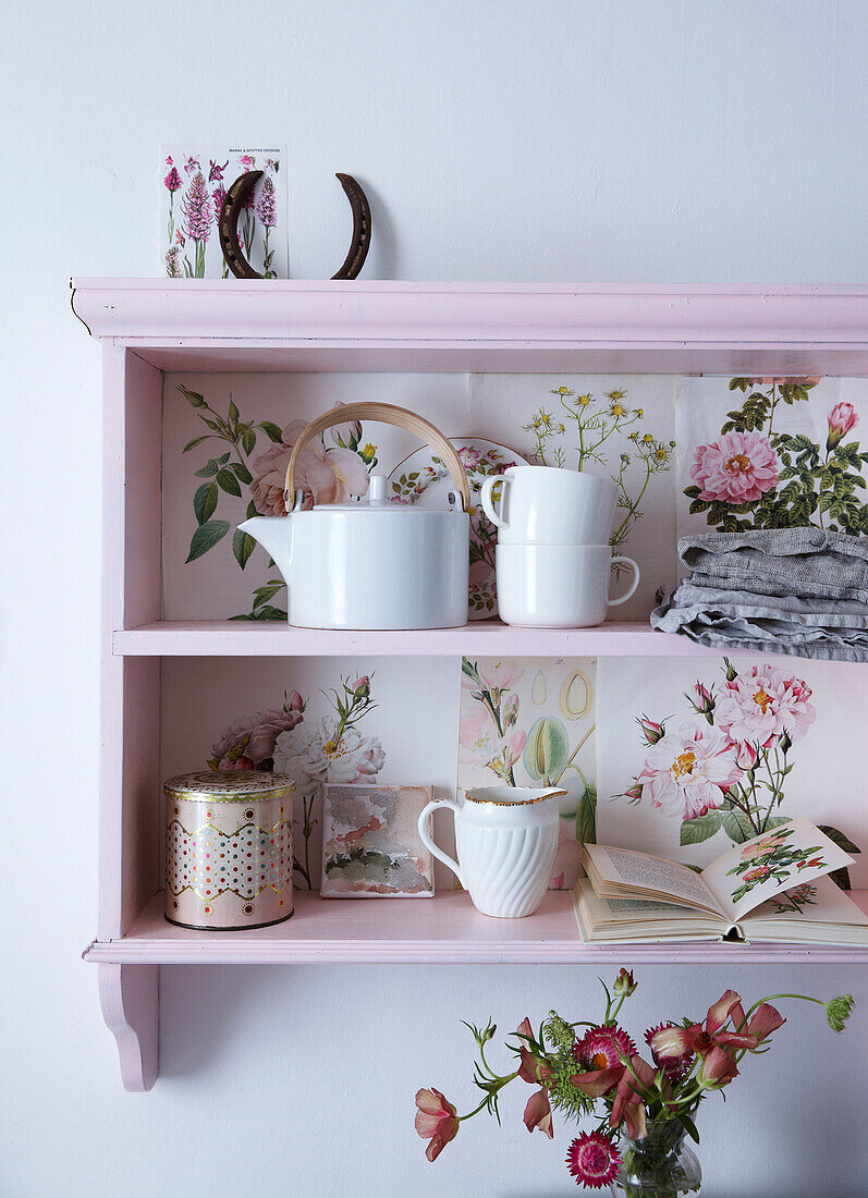Pastellrosa gestrichenes Regal mit botanischen Zeichnungen in Hufeisenform und Teekanne und Tassen mit Samenpäckchen