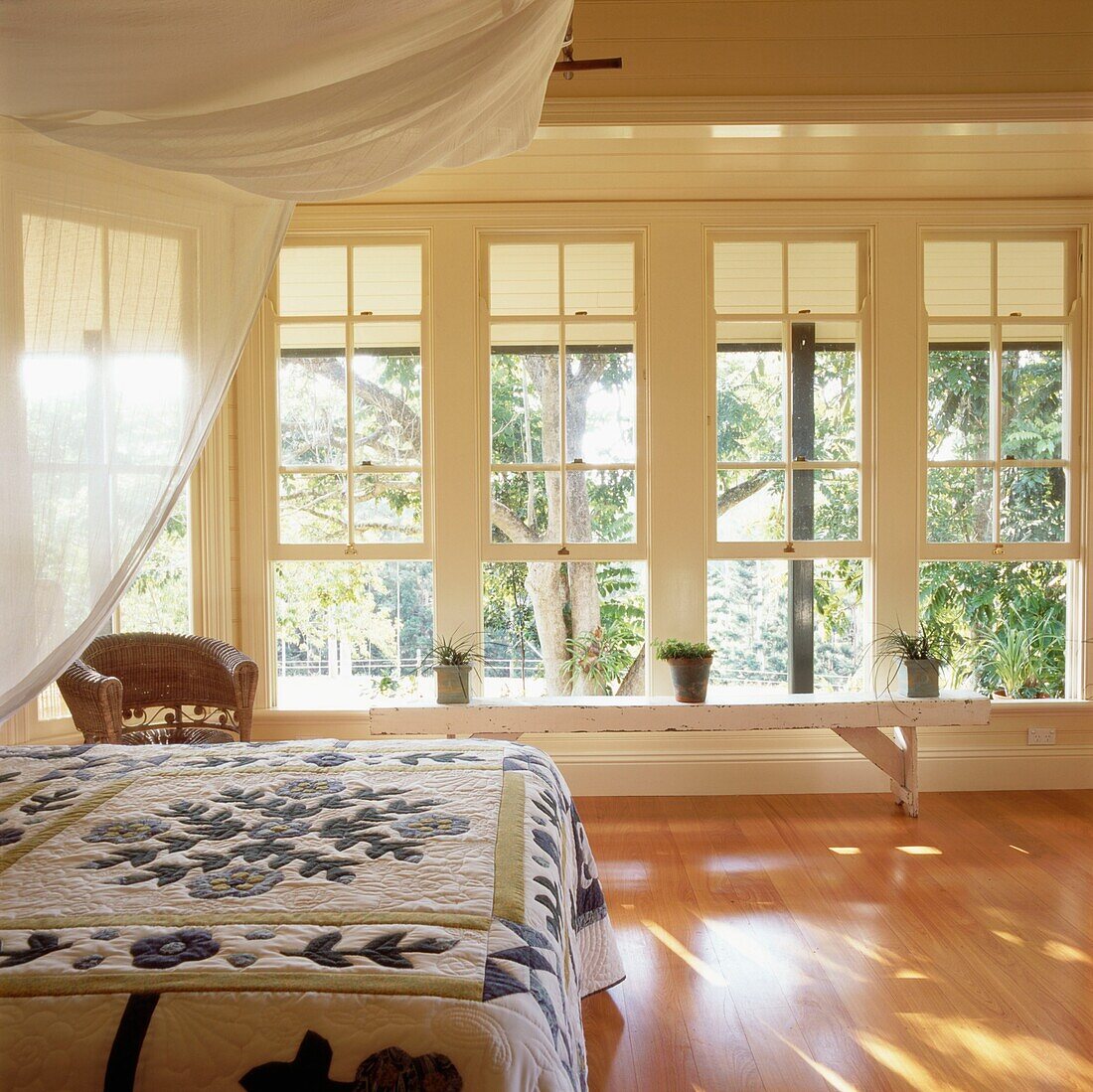 Master bedroom with wood floor and large windows double bed with patchwork quilt