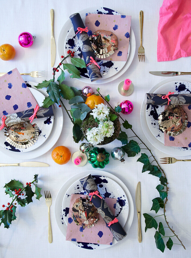 Draufsicht auf vier weihnachtlich gedeckte Tische mit Keksen, Kugeln, Stechpalmen und Efeu