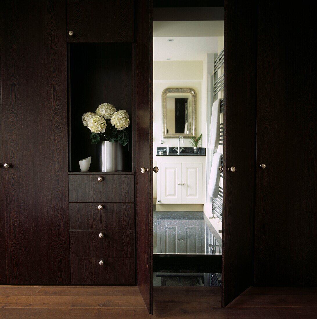 Bespoke dark wood veneer storage with view of en-suite bathroom 