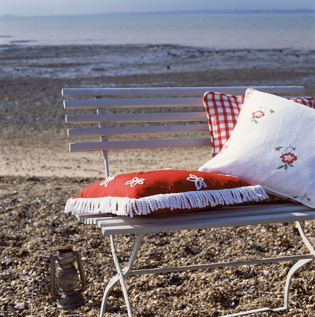 Painted wooden bench with decorative cushions on a beach