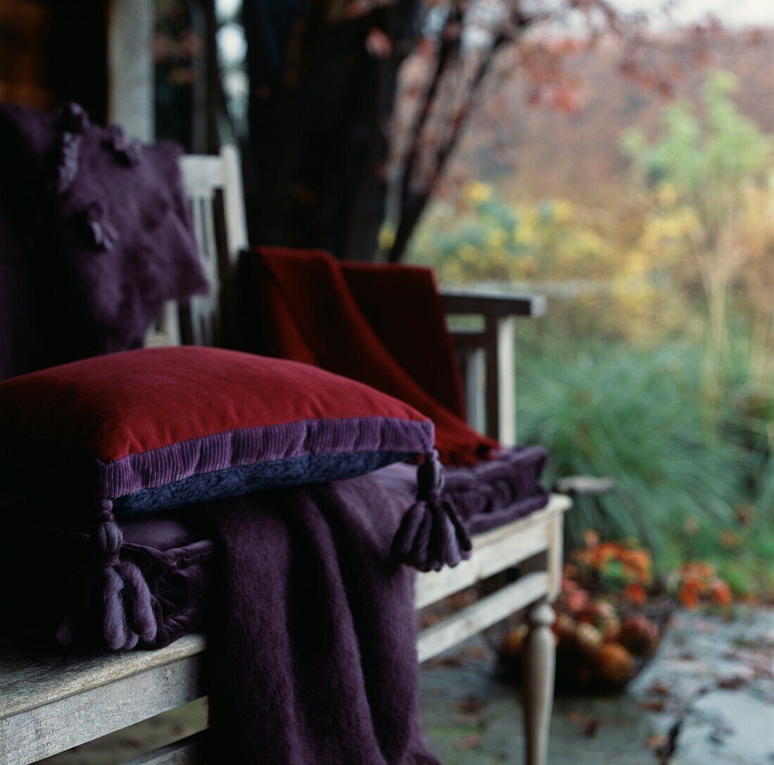 Hölzerne Gartenbank mit Decke und Kissen in einem Gartenhaus an einem herbstlichen Tag