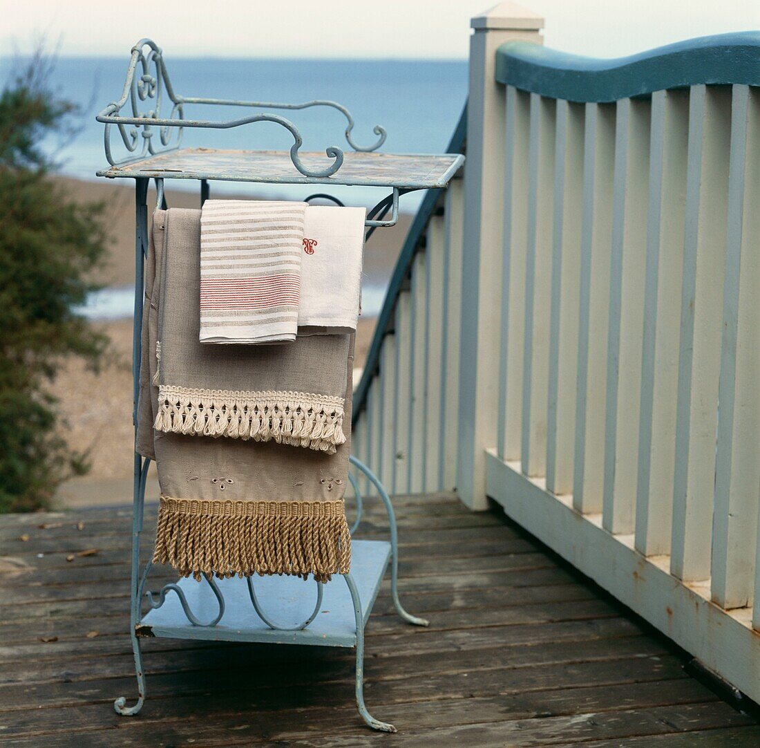 Vintage fabrics and trimmings draped on a iron work side table outside on a wooden terrace