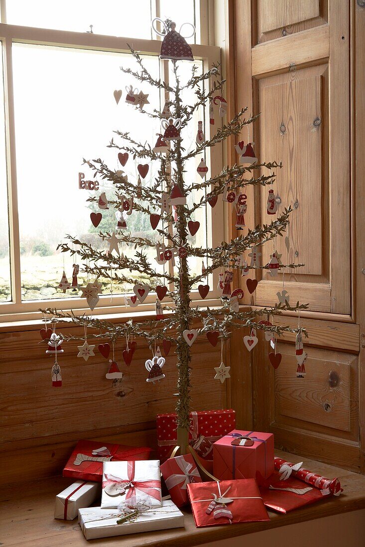 Red and white Christmas decorations on a tree surrounded by gifts on a window seat