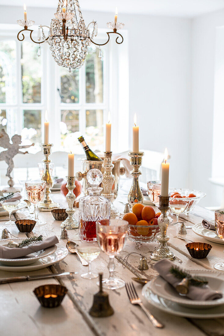 Festive table set for Christmas in white dining room with lit candles and chandelier