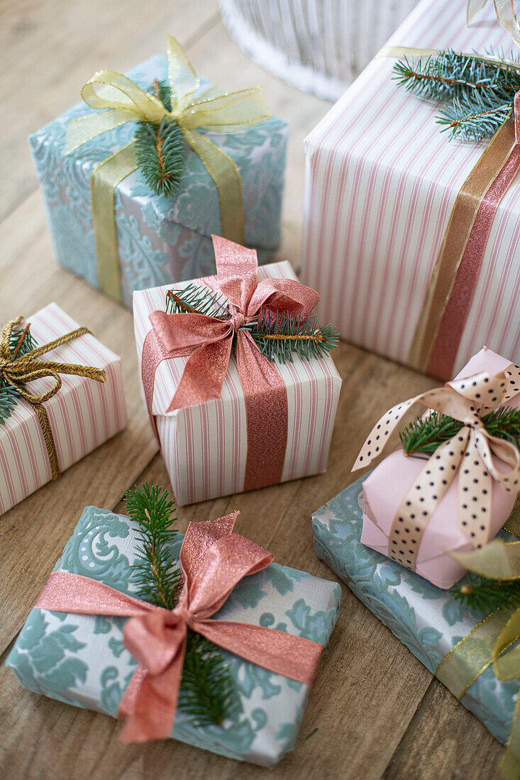 Presents giftwrapped with wallpaper and tied with ribbons and Christmas tree branches on a wooden floor underneath the tree