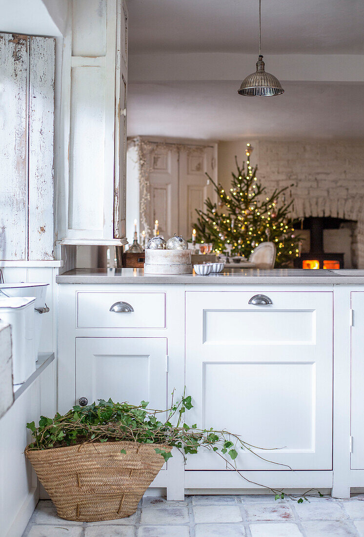 Offene Wohnküche mit einem Korb mit festlichem Laub für Girlanden, Weihnachtsbaum und Kamin im Hintergrund