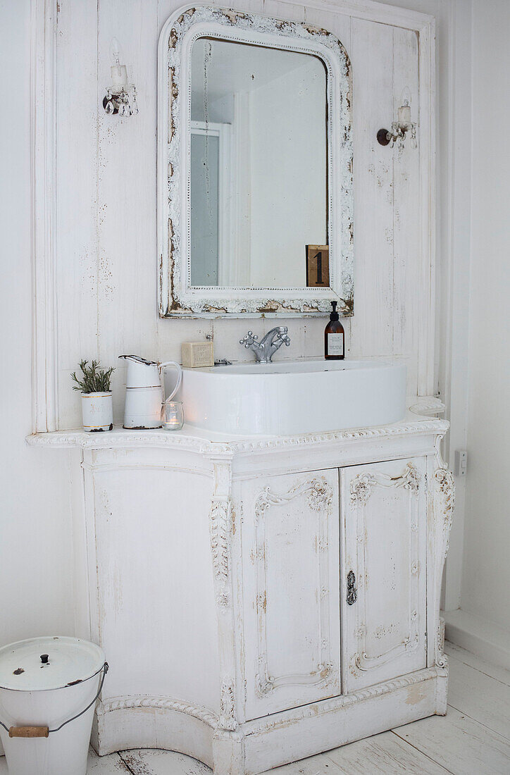 White Scandinavian style bathroom close up with ornate carved vanity unit white enamelware and pretty crystal wall lights