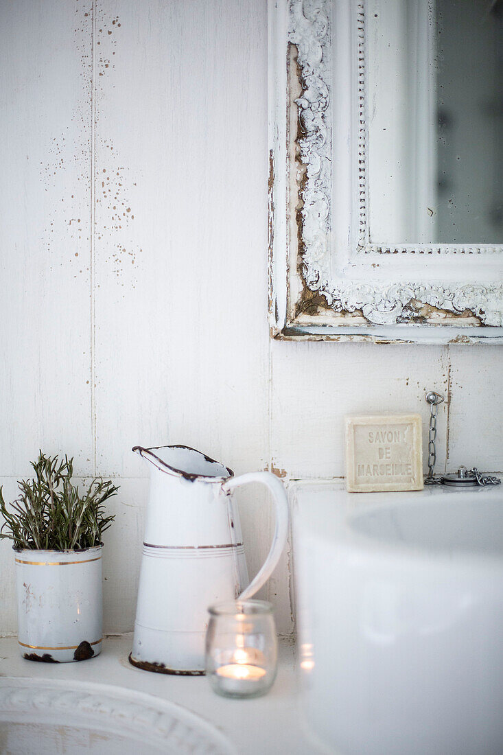 White Scandinavian style bathroom basin detail with white enamelware jug lavender pot and tealight twinkling beside a hand basin with soap beneath a white mirror