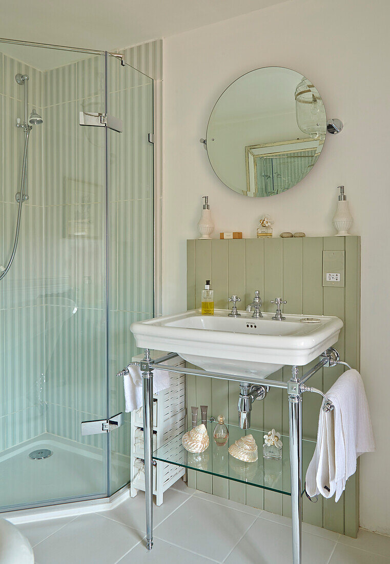 Waschbecken mit Metallgestell und runder Spiegel neben Duschkabine