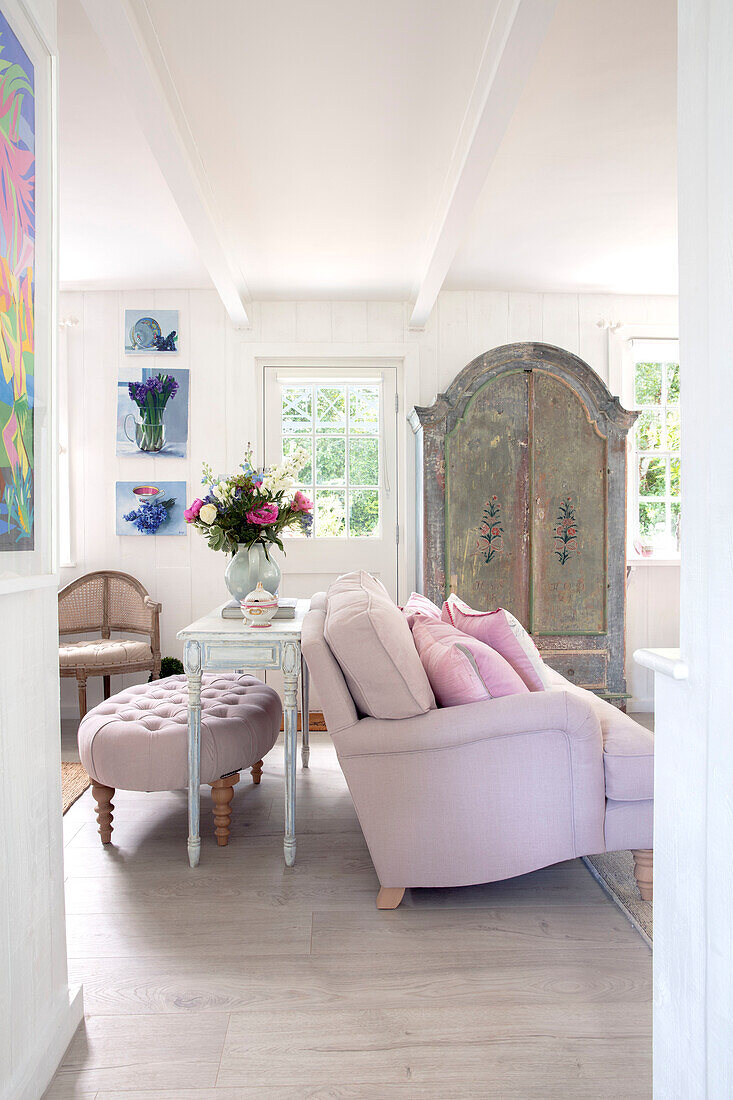 Living room with pink sofa, antique wardrobe and floral decorations