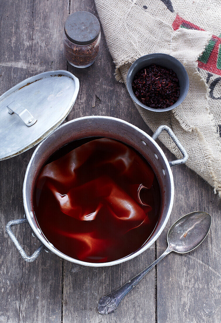 Preparation of natural dye with red leaves in a pot on a wooden surface