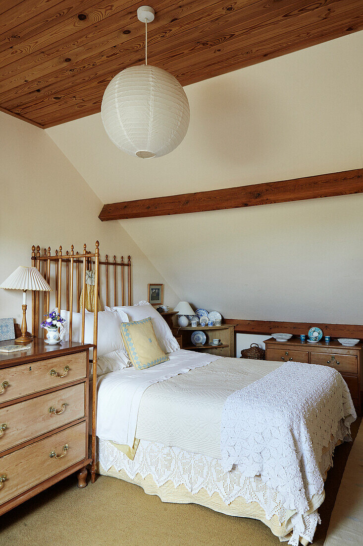 Bett mit heller Tagesdecke, daneben Kommode im Dachgeschoss-Schlafzimmer