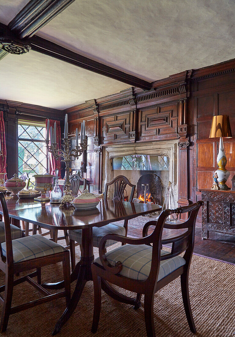 Dining table with upholstered chairs in a wood paneled walls dining room with alarge fireplace