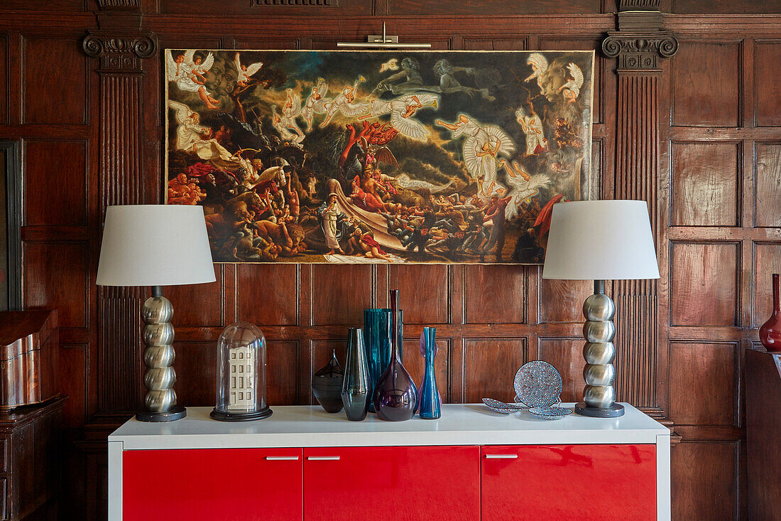 Modern sideboard with table lamps above it Paintings in the room with dark coffered panelling