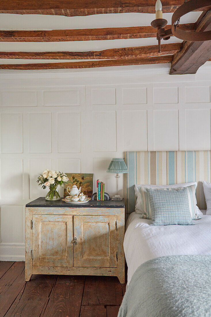 Bed with striped headboard and bedside cabinet in bedroom with coffered walls and exposed beamed ceiling