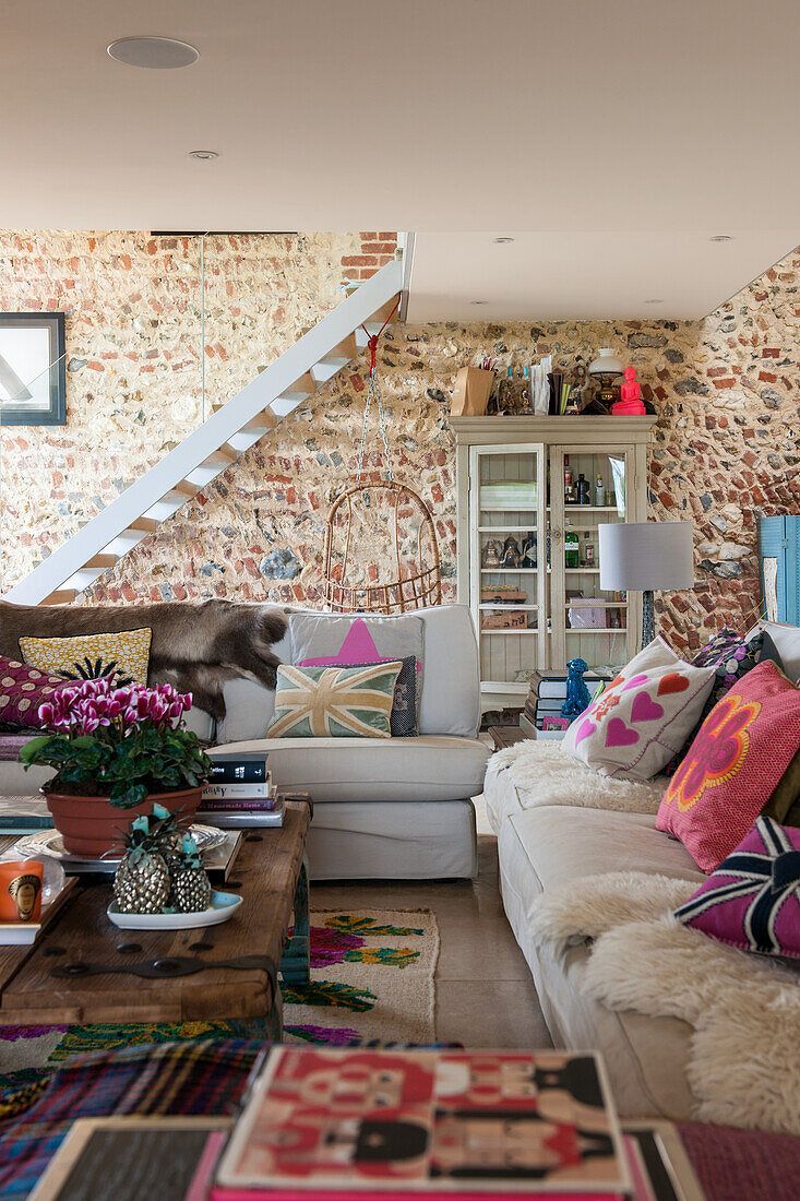 Comfortable sofas with sheepskin rugs and cushions; ladder stairs against stone wall in background