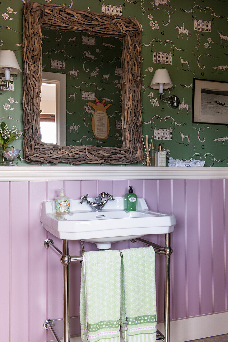 Washbasin against purple-painted wainscoting below a mirror on patterned wallpaper