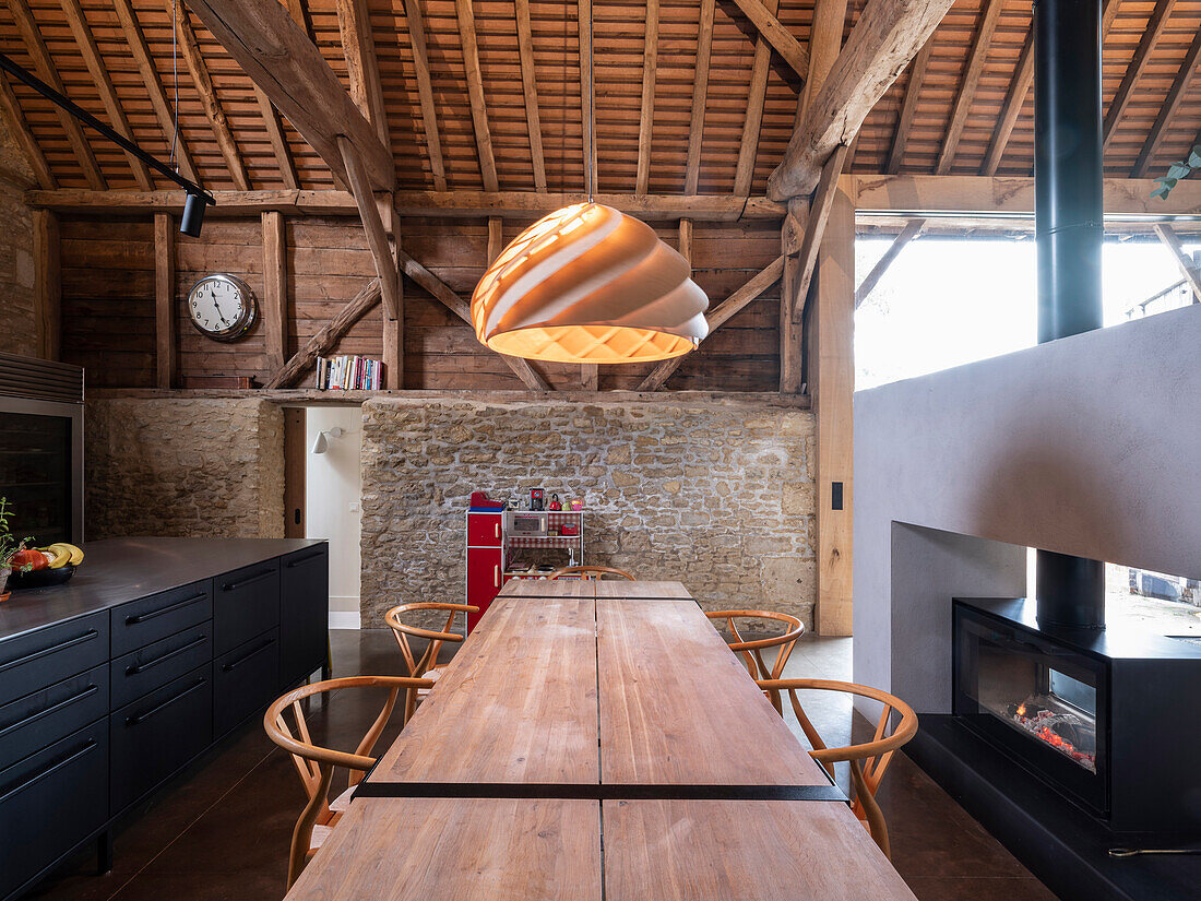 Offene Küche mit großem Esstisch und doppelseitigem Kamin in ehemaliger Scheune