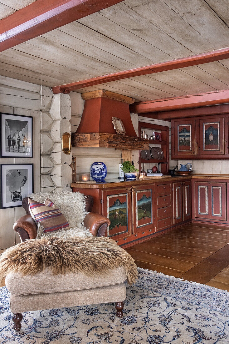 Open-plan cooking and living area in a rustic look with kitchen, armchair with stool and patterned carpet