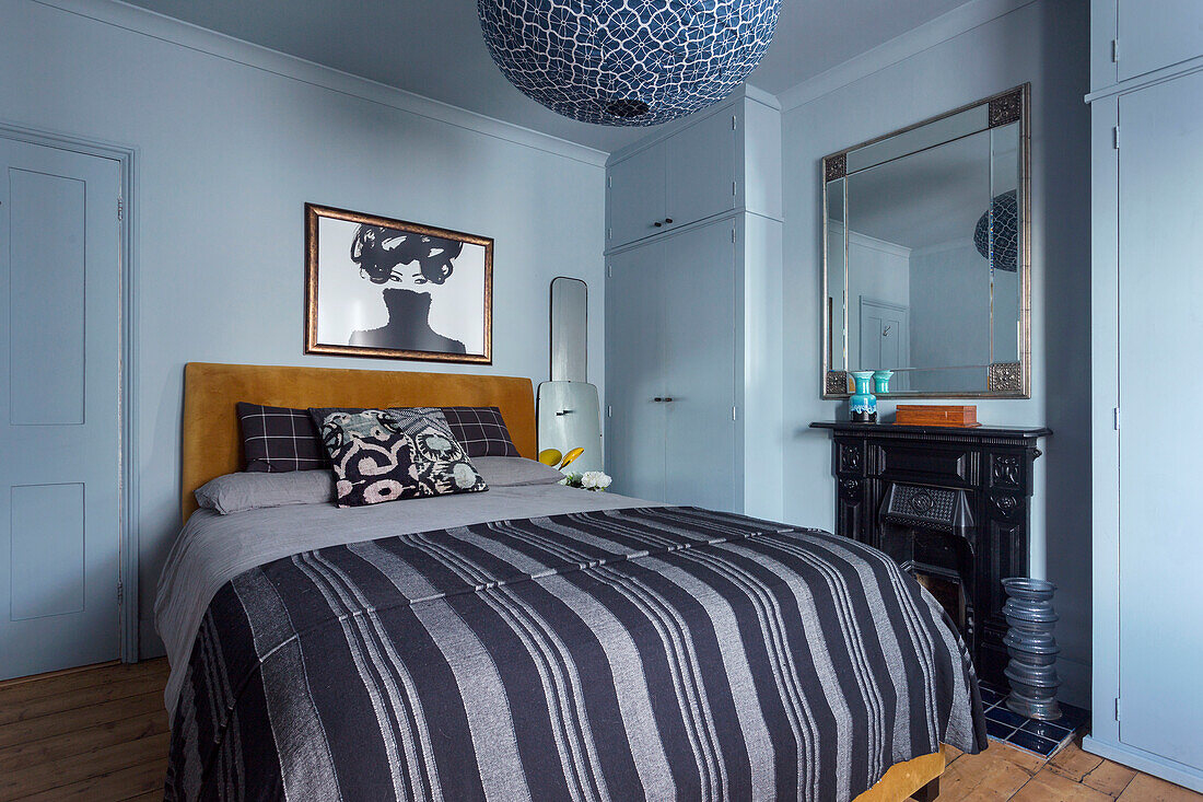 Bedroom with mustard yellow headboard, striped bedding, blue walls and fireplace