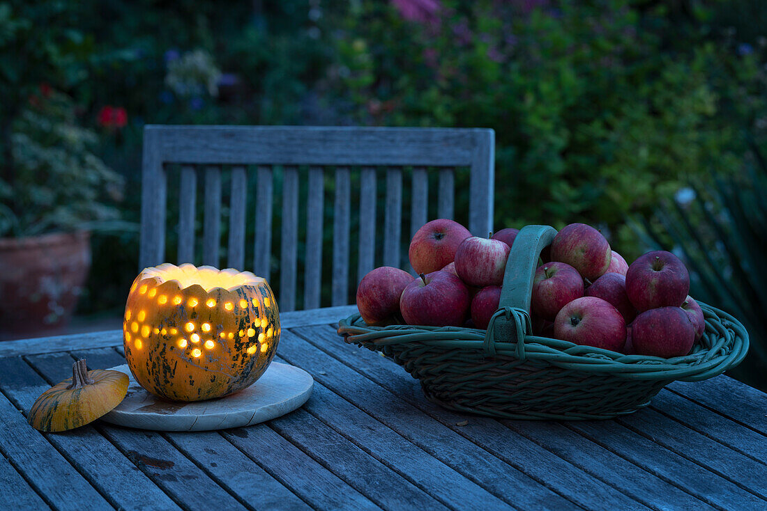 Leuchtender Kürbis und Korb mit Äpfeln auf Holztisch im Garten