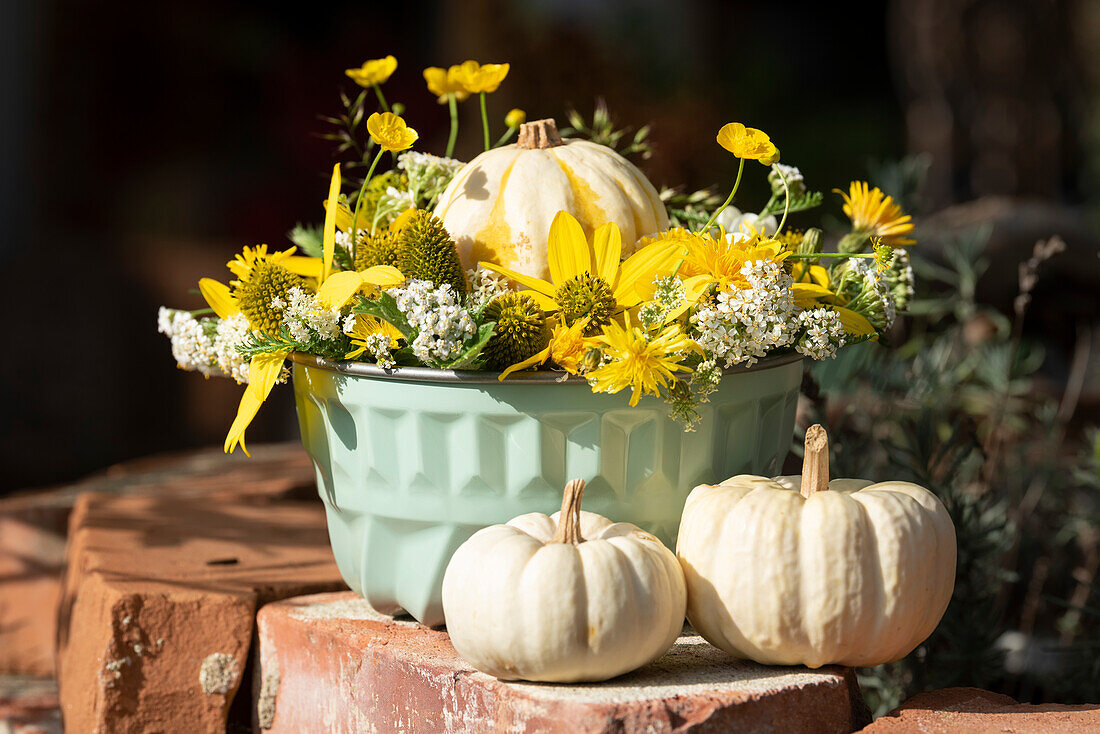 Autumn arrangement in cake pan with pumpkins and yellow flowers