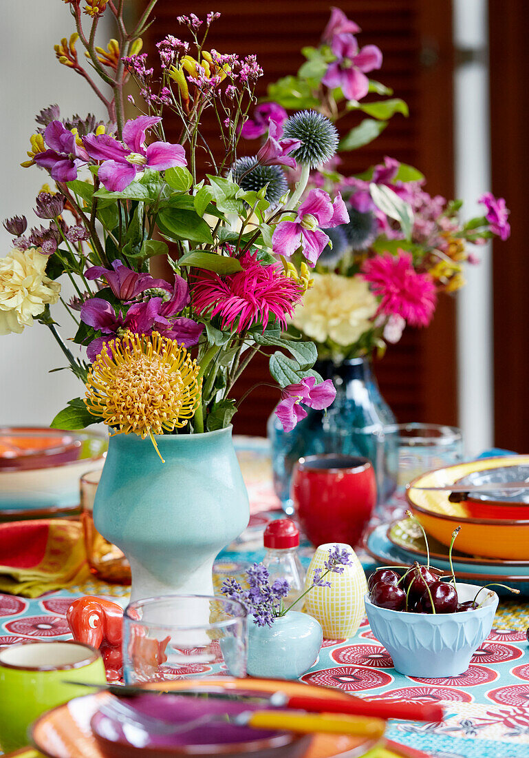 Colourful bouquet of flowers in a ceramic vase on a table with colourful crockery