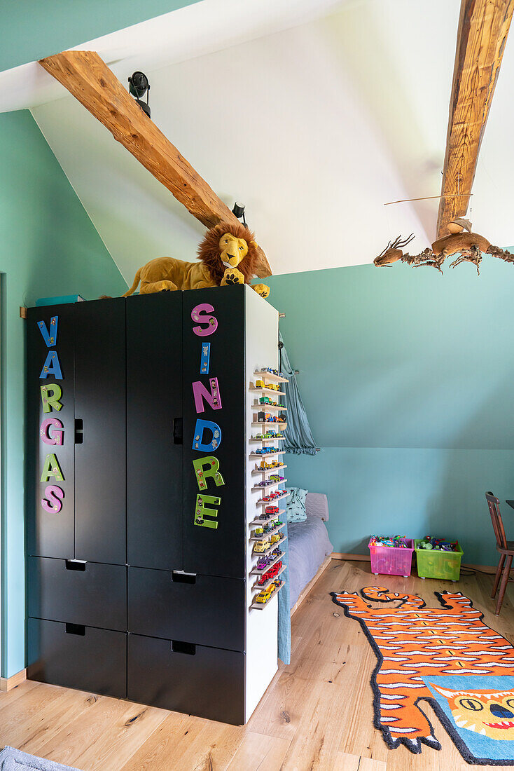 Children's room with sloping ceiling, black wardrobe, colourful rug and toy storage