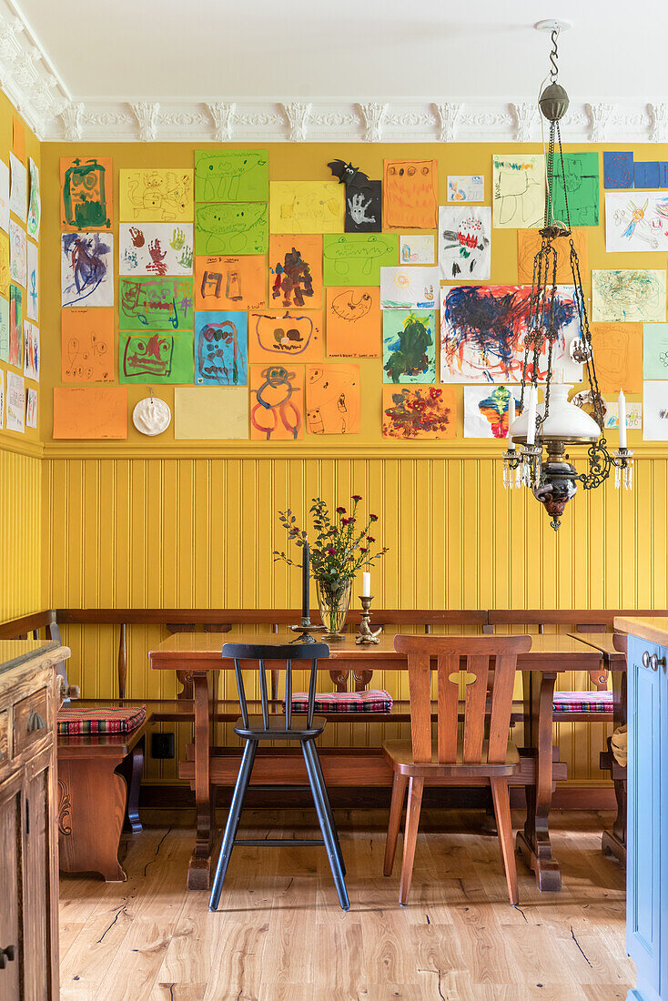 Creative dining room with wooden furniture and children's art on the yellow wall