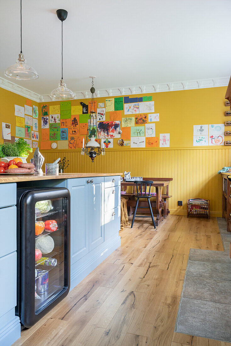 Kücheninterieur mit blauen Schränken, und gelber Wand mit Kinderzeichnungen