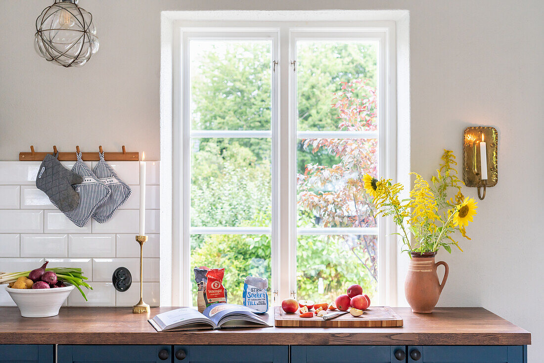 Kitchen window with view of greenery, vase with sunflowers and fresh fruit