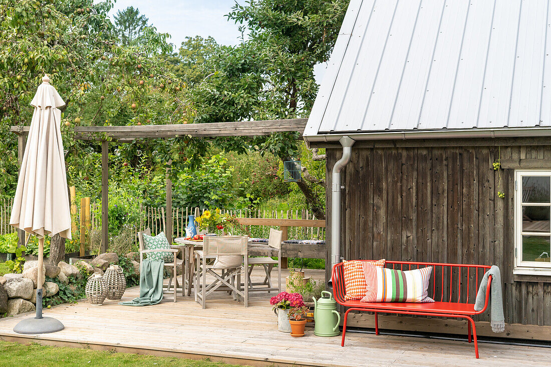 Terrasse mit Holzdeck, Gartenmöbeln und farbigen Kissen vor einem Holzhaus