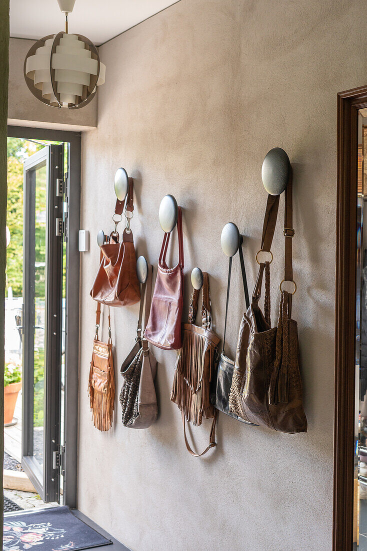 Leather handbags on wall hooks in the entrance area with pendant light