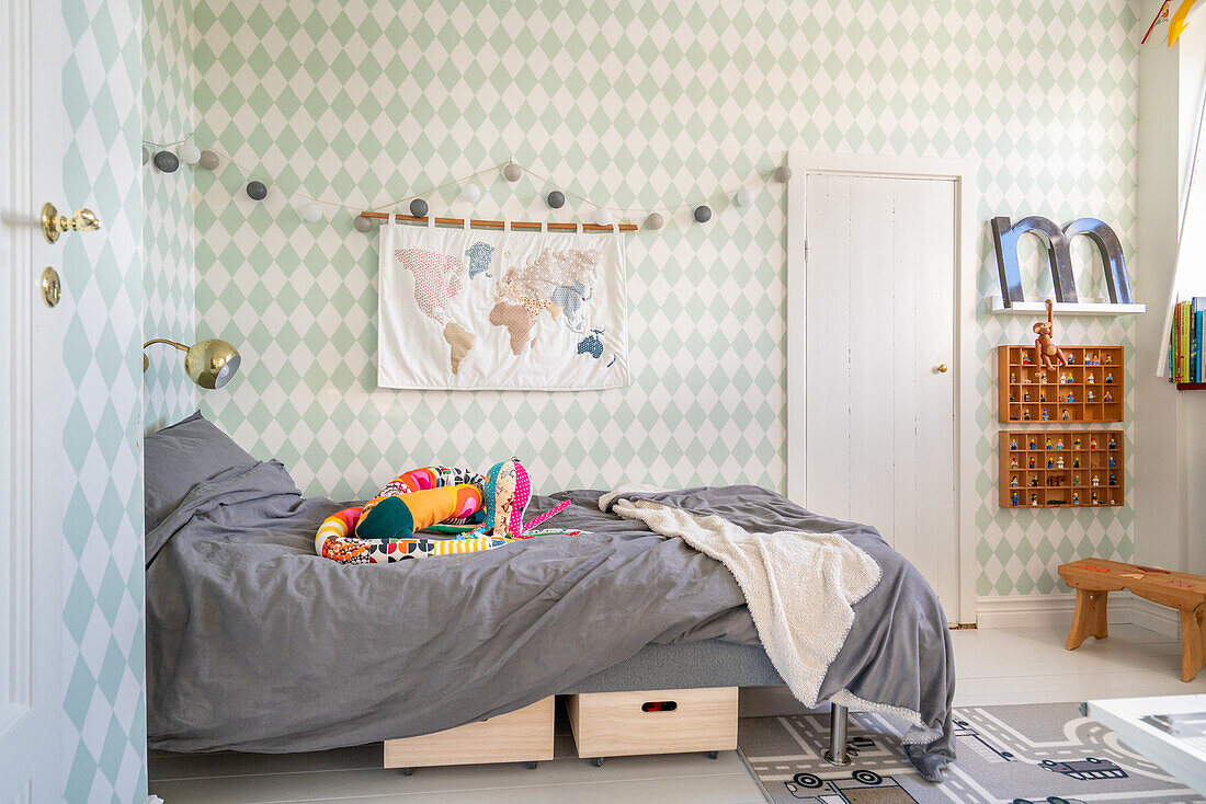 Tapete mit Rautenmuster, Bett mit bunter Kuschelschlange und Spielteppich in Kinderzimmer