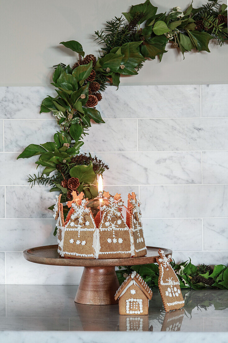Candle in a cake with gingerbread houses in front of green wreath