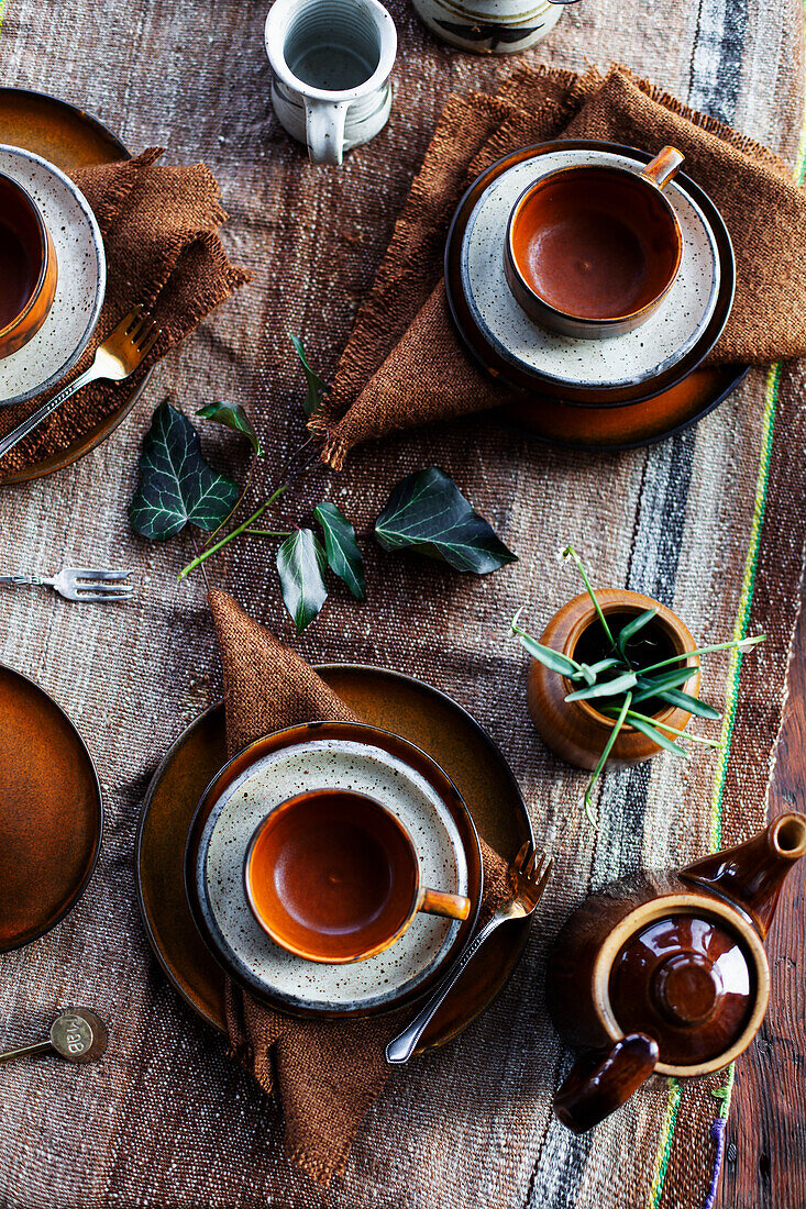 Rustic breakfast table with brown ceramic crockery and plant leaves