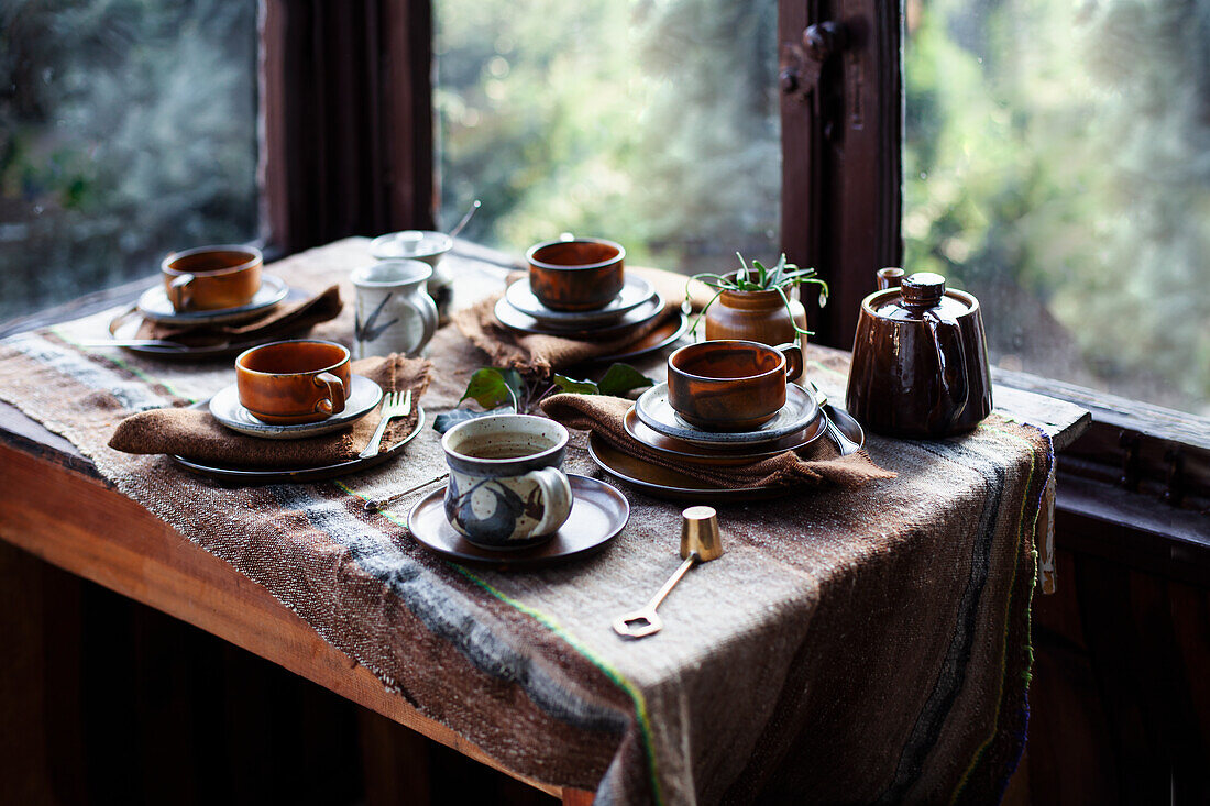 Set wooden table with ceramic cups and teapot by the window