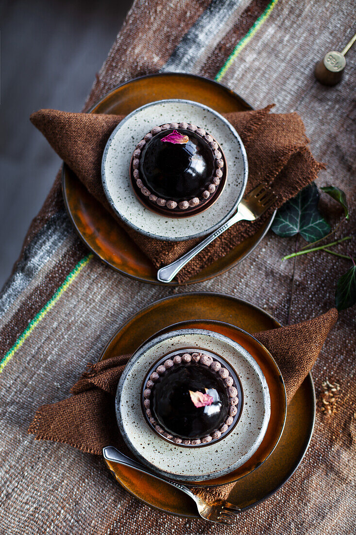 Zwei Dessertteller mit dunklen Schokoladenmousse-Kugeln und Blüten auf rustikalem Tischtuch