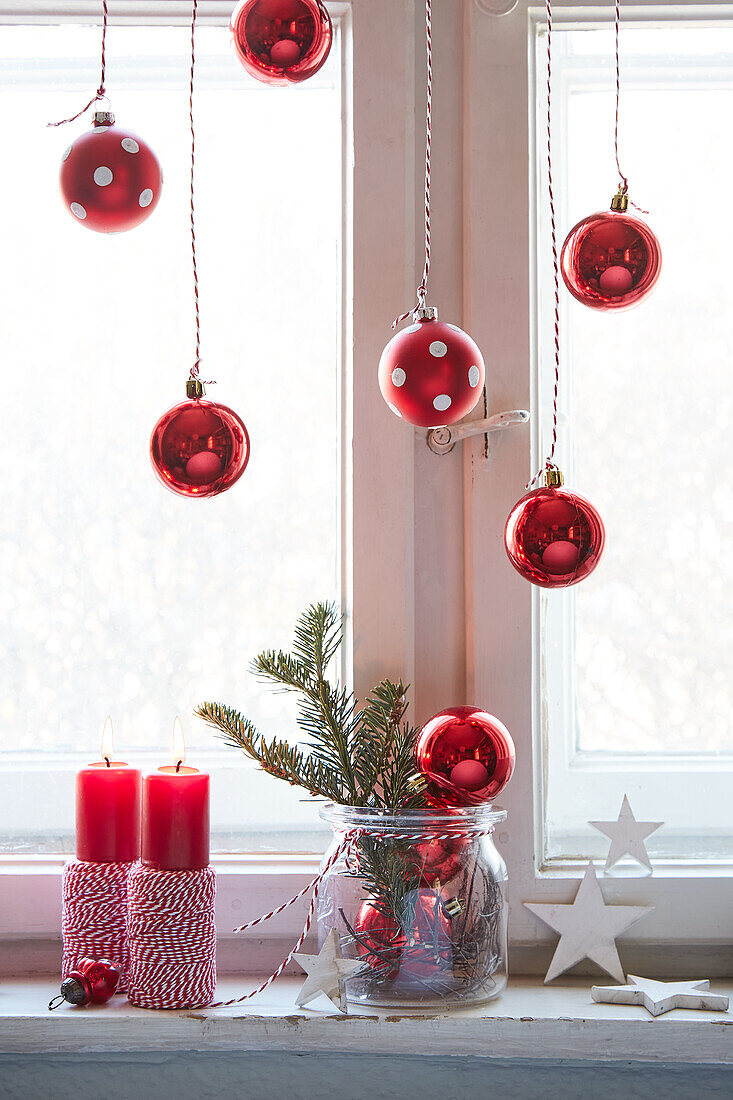 Red Christmas baubles, candles and fir branches in a jar as window decorations